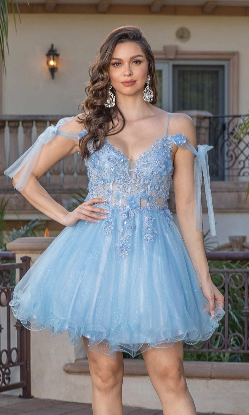 A woman stands outdoors in the Sheer-Corset Short Babydoll Hoco Dress 3339, a light blue tulle homecoming dress with floral appliqués, styled with large earrings.